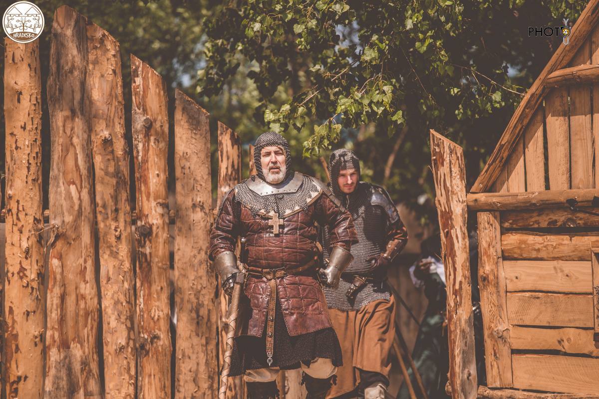 Inštruktor v brnení a kovanici za drevenou palisádou